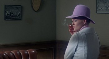 Movie still from “The Thomas Crown Affair” (1968), directed by Norman Jewison – A woman wearing a purple hat smoking a cigarette; Medium shot, Over the shoulder angle