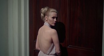 Movie still from “The Thomas Crown Affair” (1968), directed by Norman Jewison – A woman in a white dress standing in front of a door; Medium shot, Over the shoulder angle