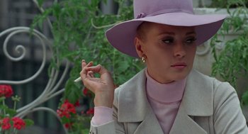 Movie still from “The Thomas Crown Affair” (1968), directed by Norman Jewison – A woman in a purple hat holding a cigarette in her hand; Close Up shot, Over the shoulder angle