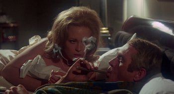 Movie still from “The Thomas Crown Affair” (1968), directed by Norman Jewison – A woman smoking a cigarette while a man lies in bed; Medium shot, High angle