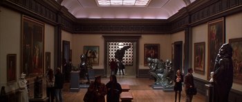 Movie still from “The Thomas Crown Affair” (1999), directed by John McTiernan – A group of people sitting in a room with sculptures; Wide shot, High angle