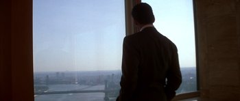 Movie still from “The Thomas Crown Affair” (1999), directed by John McTiernan – A man in a suit looking out of a window; Medium shot, Over the shoulder angle