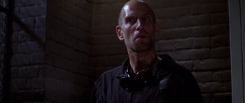 Movie still from “The Thomas Crown Affair” (1999), directed by John McTiernan – A bald man wearing a black shirt and headphones; Close Up shot, Low angle