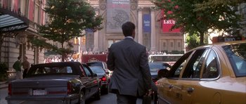 Movie still from “The Thomas Crown Affair” (1999), directed by John McTiernan – A man in a suit is walking down the street; Wide shot, Over the shoulder angle