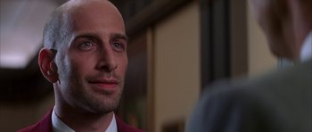 Movie still from “The Thomas Crown Affair” (1999), directed by John McTiernan – A man in a red jacket is looking at the camera; Close Up shot, Over the shoulder angle