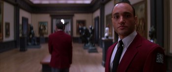 Movie still from “The Thomas Crown Affair” (1999), directed by John McTiernan – A man in a red jacket standing next to a statue; Medium shot, Low angle