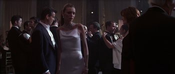 Movie still from “The Thomas Crown Affair” (1999), directed by John McTiernan – A woman in a white dress standing in front of a group of people; Medium shot, Low angle
