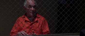 Movie still from “The Thomas Crown Affair” (1999), directed by John McTiernan – An older man in a red shirt is behind a fence; Close Up shot, High angle