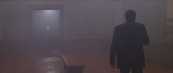 Movie still from “The Thomas Crown Affair” (1999), directed by John McTiernan – A man in a suit standing in front of a bench in a room; Wide shot, Over the shoulder angle