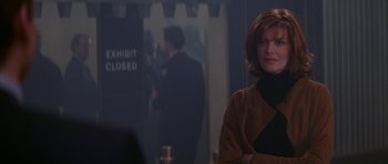 Movie still from “The Thomas Crown Affair” (1999), directed by John McTiernan – A woman standing in front of an exhibit with people in the background; Medium shot, Over the shoulder angle