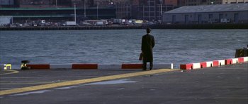 Movie still from “The Thomas Crown Affair” (1999), directed by John McTiernan – A man standing on a pier near a body of water; Extreme Wide shot, High angle
