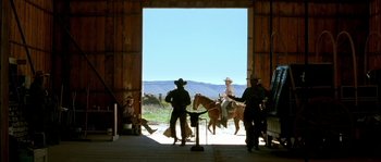 Movie still from “The Three Burials of Melquiades Estrada” (2005), directed by Tommy Lee Jones – A group of people riding horses in a barn; Wide shot, Low angle