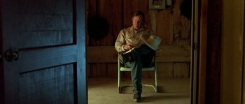 Movie still from “The Three Burials of Melquiades Estrada” (2005), directed by Tommy Lee Jones – A man sitting on a chair in a room; Medium shot, High angle