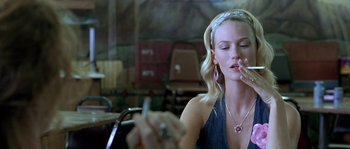 Movie still from “The Three Burials of Melquiades Estrada” (2005), directed by Tommy Lee Jones – A woman sitting at a table smoking a cigarette and looking at her cell phone; Close Up shot, Over the shoulder angle