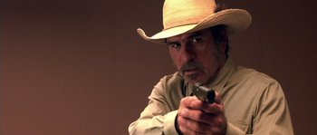 Movie still from “The Three Burials of Melquiades Estrada” (2005), directed by Tommy Lee Jones – A man in a straw cowboy hat holding a gun; Close Up shot, Over the shoulder angle