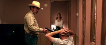 Movie still from “The Three Burials of Melquiades Estrada” (2005), directed by Tommy Lee Jones – A man holding a gun in front of a woman in front of a mirror; Medium shot, Over the shoulder angle