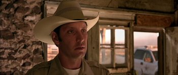 Movie still from “The Three Burials of Melquiades Estrada” (2005), directed by Tommy Lee Jones – A man wearing a cowboy hat in front of a window; Close Up shot, Over the shoulder angle