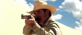 Movie still from “The Three Burials of Melquiades Estrada” (2005), directed by Tommy Lee Jones – A man in a cowboy hat is holding a gun; Close Up shot, Over the shoulder angle