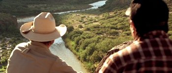 Movie still from “The Three Burials of Melquiades Estrada” (2005), directed by Tommy Lee Jones – A man wearing a cowboy hat looking out over a river; Extreme Wide shot, Over the shoulder angle