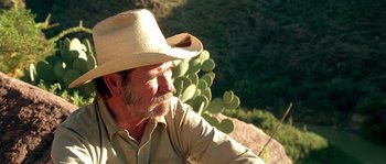 Movie still from “The Three Burials of Melquiades Estrada” (2005), directed by Tommy Lee Jones – An older man wearing a cowboy hat with a cactus in the background; Close Up shot, Over the shoulder angle