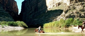 Movie still from “The Three Burials of Melquiades Estrada” (2005), directed by Tommy Lee Jones – A man riding a horse through a river; Extreme Wide shot, High angle