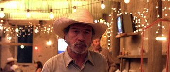 Movie still from “The Three Burials of Melquiades Estrada” (2005), directed by Tommy Lee Jones – An older man wearing a cowboy hat in front of lights; Close Up shot, Over the shoulder angle