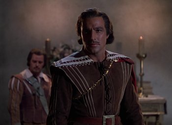 Movie still from “The Three Musketeers” (1948), directed by George Sidney – A man in a brown and white outfit standing in front of candles; Medium shot, Over the shoulder angle