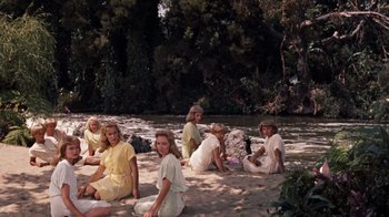 Movie still from “The Time Machine” (1960), directed by George Pal – A group of women sitting on the sand near a body of water; Wide shot, High angle