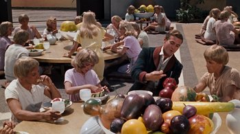 Movie still from “The Time Machine” (1960), directed by George Pal – A group of people sitting around a table with fruit; Wide shot, High angle