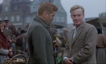 Movie still from “The Tin Drum” (1979), directed by Volker Schlöndorff – Two men standing next to each other holding mushrooms; Medium shot, Over the shoulder angle