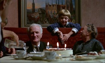 Movie still from “The Tin Drum” (1979), directed by Volker Schlöndorff – A man and a boy sitting in front of a birthday cake; Medium shot, Over the shoulder angle