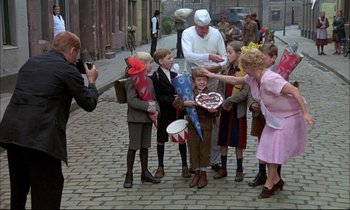 Movie still from “The Tin Drum” (1979), directed by Volker Schlöndorff – A group of people standing on a brick street; Wide shot, High angle