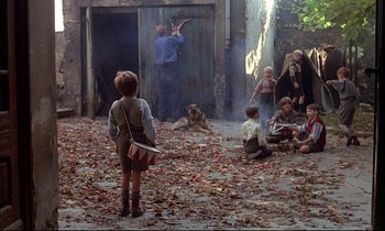 Movie still from “The Tin Drum” (1979), directed by Volker Schlöndorff – A group of children sitting in the dirt; Wide shot, Over the shoulder angle