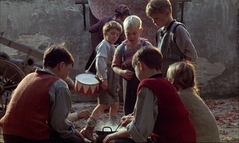 Movie still from “The Tin Drum” (1979), directed by Volker Schlöndorff – A group of young children playing with a toy drum; Medium shot, High angle