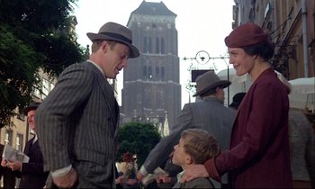 Movie still from “The Tin Drum” (1979), directed by Volker Schlöndorff – A group of people standing next to each other on a street; Medium shot, Over the shoulder angle