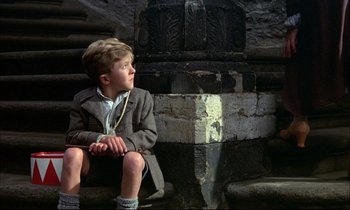 Movie still from “The Tin Drum” (1979), directed by Volker Schlöndorff – A young boy sitting on a stone steps; Medium shot, Low angle