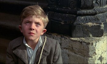 Movie still from “The Tin Drum” (1979), directed by Volker Schlöndorff – A young boy wearing a suit sitting on a ledge; Close Up shot, Low angle