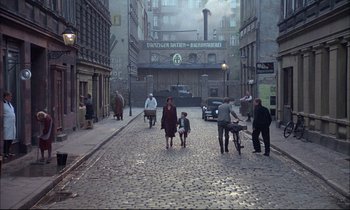 Movie still from “The Tin Drum” (1979), directed by Volker Schlöndorff – A group of people walking down a street; Extreme Wide shot, High angle