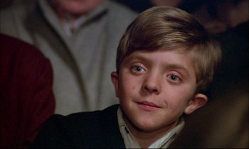 Movie still from “The Tin Drum” (1979), directed by Volker Schlöndorff – A young boy with blue eyes sitting in front of an audience; Close Up shot, Low angle