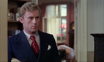 Movie still from “The Tin Drum” (1979), directed by Volker Schlöndorff – A man wearing a suit and tie standing in front of a camera; Close Up shot, Over the shoulder angle