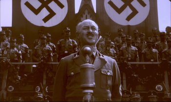 Movie still from “The Tin Drum” (1979), directed by Volker Schlöndorff – An old photo of a man in a military uniform speaking; Medium shot, High angle