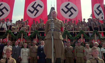 Movie still from “The Tin Drum” (1979), directed by Volker Schlöndorff – A group of men and women standing in front of a flag; Wide shot, Low angle