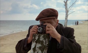 Movie still from “The Tin Drum” (1979), directed by Volker Schlöndorff – A man taking a picture of the ocean with a camera; Close Up shot, Over the shoulder angle
