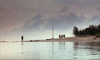 Movie still from “The Tin Drum” (1979), directed by Volker Schlöndorff – A group of people standing on a beach near the water; Extreme Wide shot, Low angle