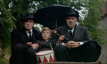 Movie still from “The Tin Drum” (1979), directed by Volker Schlöndorff – A group of men sitting next to each other holding umbrellas; Medium shot, Low angle