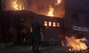 Movie still from “The Tin Drum” (1979), directed by Volker Schlöndorff – A man standing in front of a burning building; Extreme Wide shot, Low angle