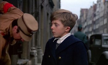 Movie still from “The Tin Drum” (1979), directed by Volker Schlöndorff – A young boy wearing a suit and hat; Close Up shot, Over the shoulder angle