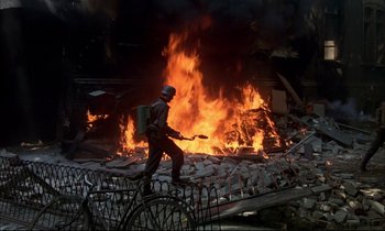 Movie still from “The Tin Drum” (1979), directed by Volker Schlöndorff – A person walking on a pile of rubble near a fire; Wide shot, High angle