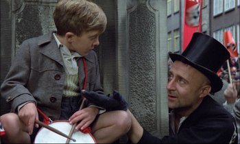 Movie still from “The Tin Drum” (1979), directed by Volker Schlöndorff – A man sitting next to a boy with a drum; Medium shot, Over the shoulder angle