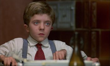 Movie still from “The Tin Drum” (1979), directed by Volker Schlöndorff – A young boy sitting at a dinner table looking sad; Close Up shot, Low angle